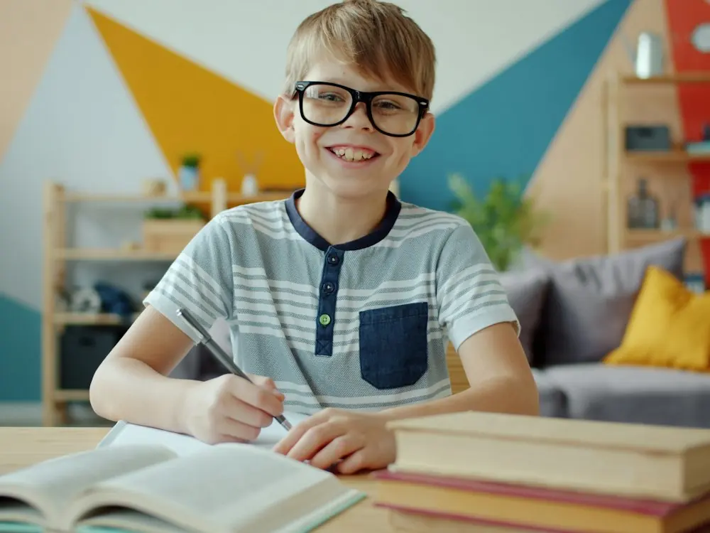 A smiling boy with glasses studying at a desk
