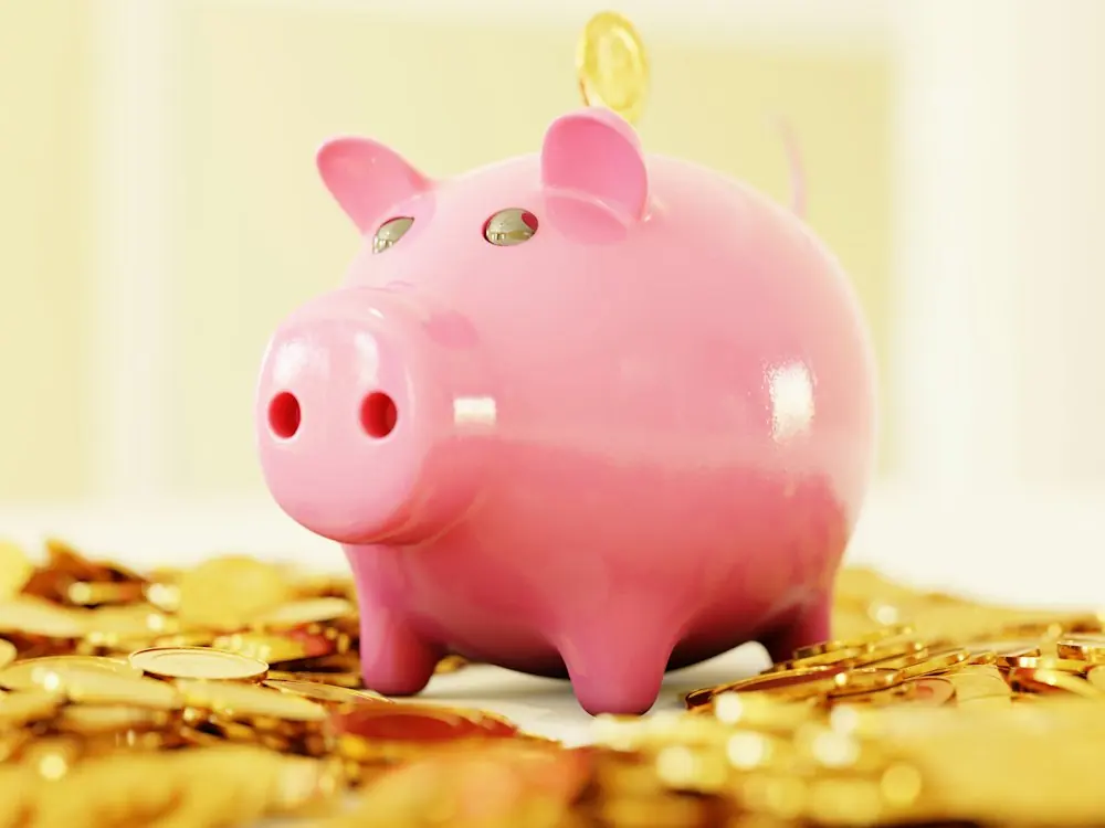 A pink piggy bank sitting on a pile of gold coins